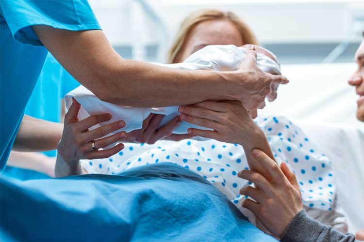 Midwife passing baby to mother after birth | Image