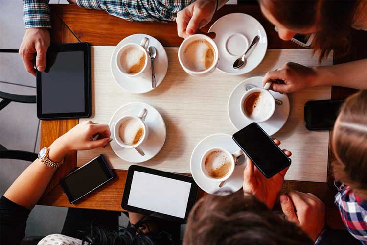 Vertical view of a group gathered drinking coffee and using technology | Image