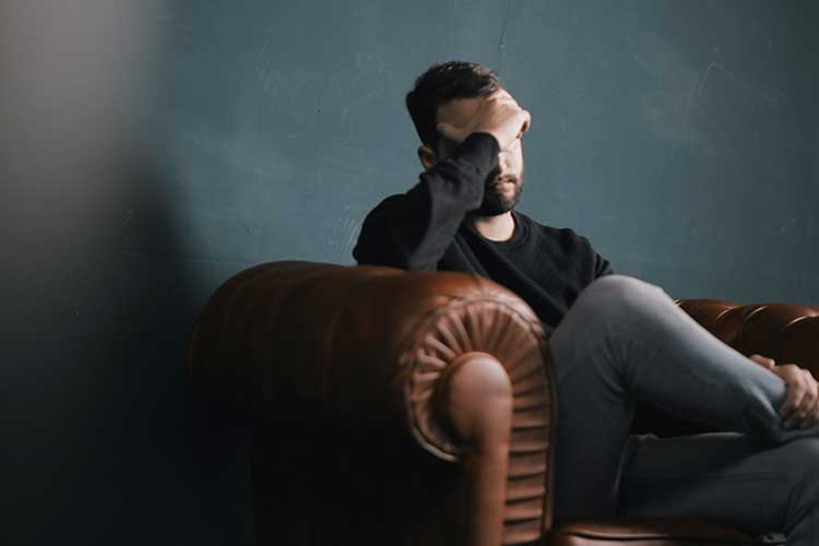 Upset man with hand on head sitting in chair