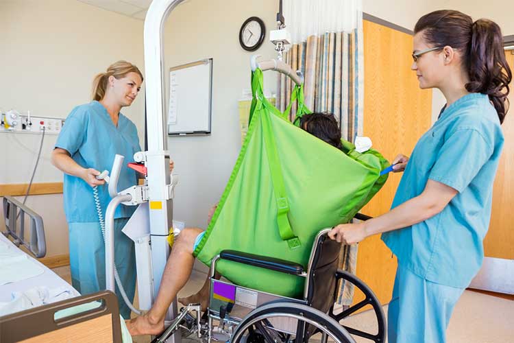 Nurses aiding patient into wheelchair with assistive device