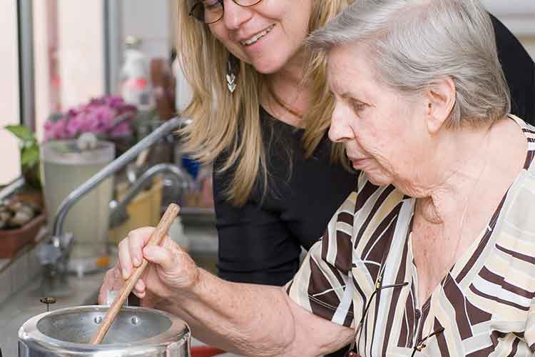 Elderly woman cooking with support of another woman | Image