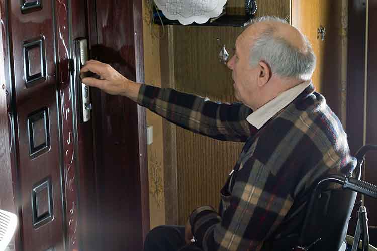 Elderly male in wheelchair opening a door | Image