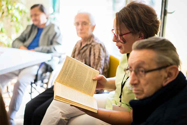 Woman reading a book to elderly people | Image