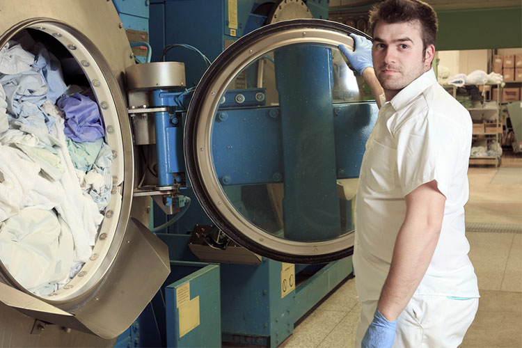 man working in aged care facility or hospital cleaning laundry with industrial machine