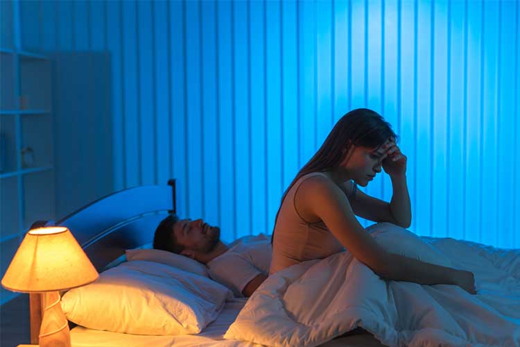 Woman awake in bed next to her partner