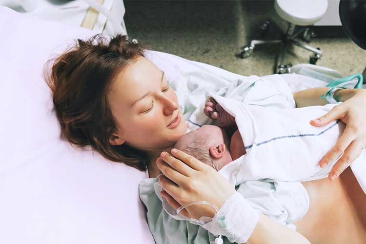 Woman holding her newborn baby in hospital | Image
