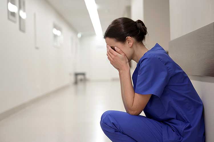 Nurse sitting in corridor with hands on face | Image