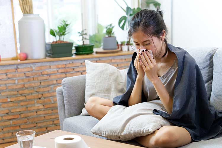 Woman with a cold blowing her nose sitting on the couch | Image