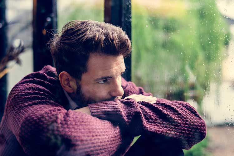 Sad man looking out the window on a rainy day | Image