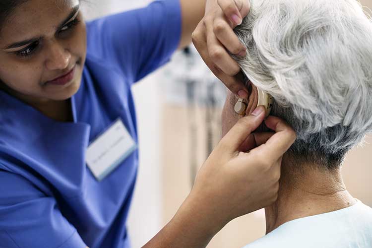 hearing specialist inserting hearing aid into older woman's ear